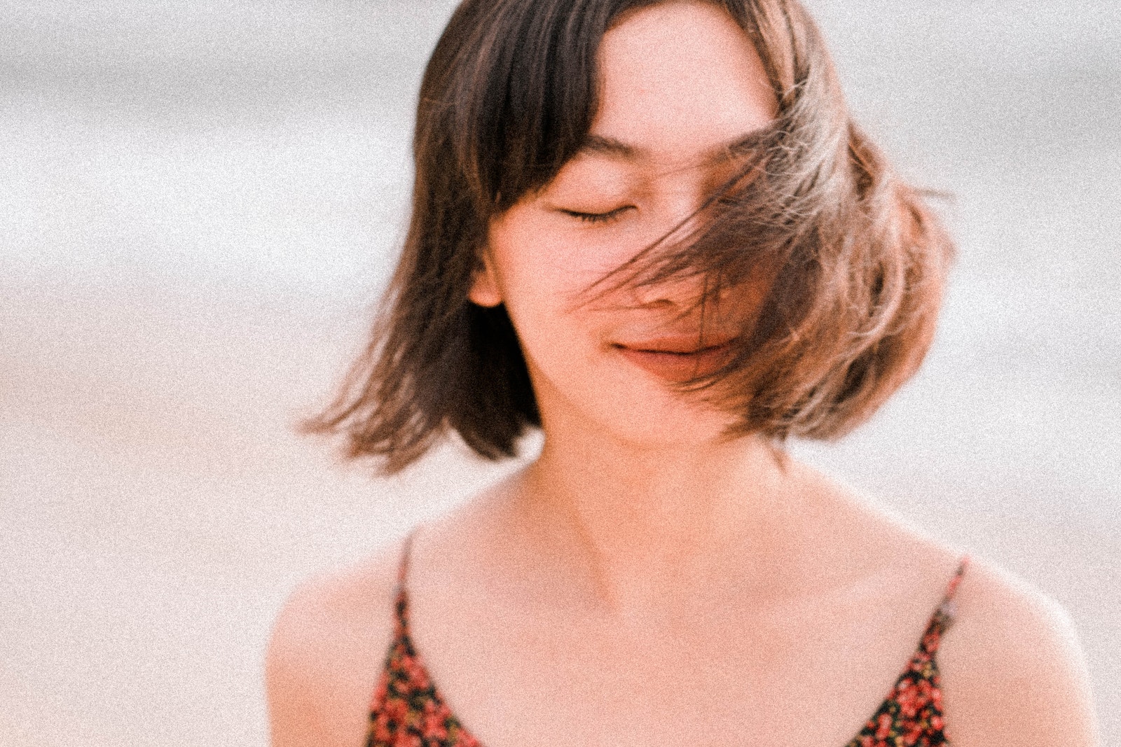 Charming Asian woman with short brown hair closing eyes and waving with hair in wind