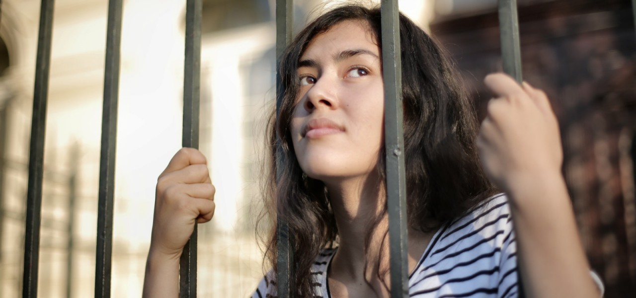 Sad isolated young woman looking away through fence with hope