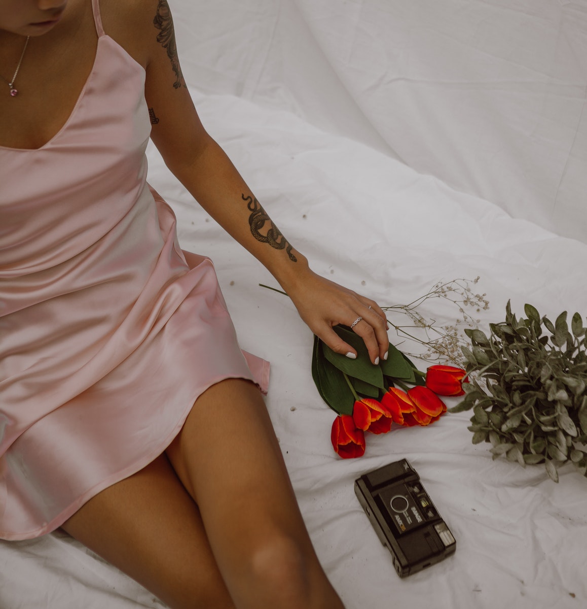 Crop alluring woman sitting on bed with flowers and retro photo camera