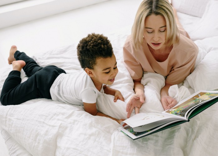 Mother and Son Reading Book Together while Lying on a Bed with White Blanket