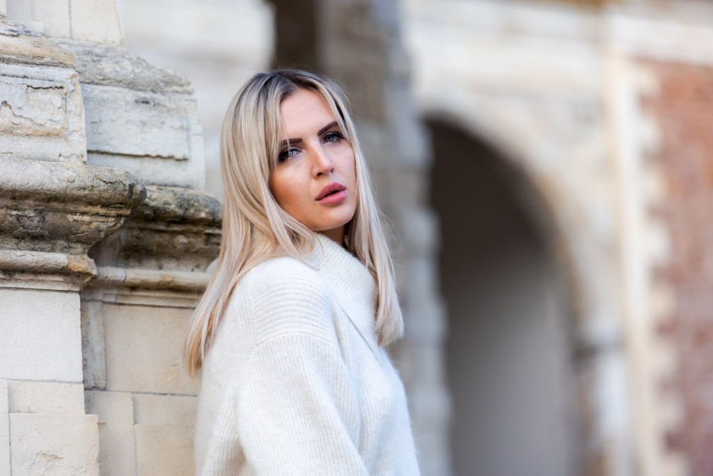 woman in white sweater standing near white concrete wall during daytime