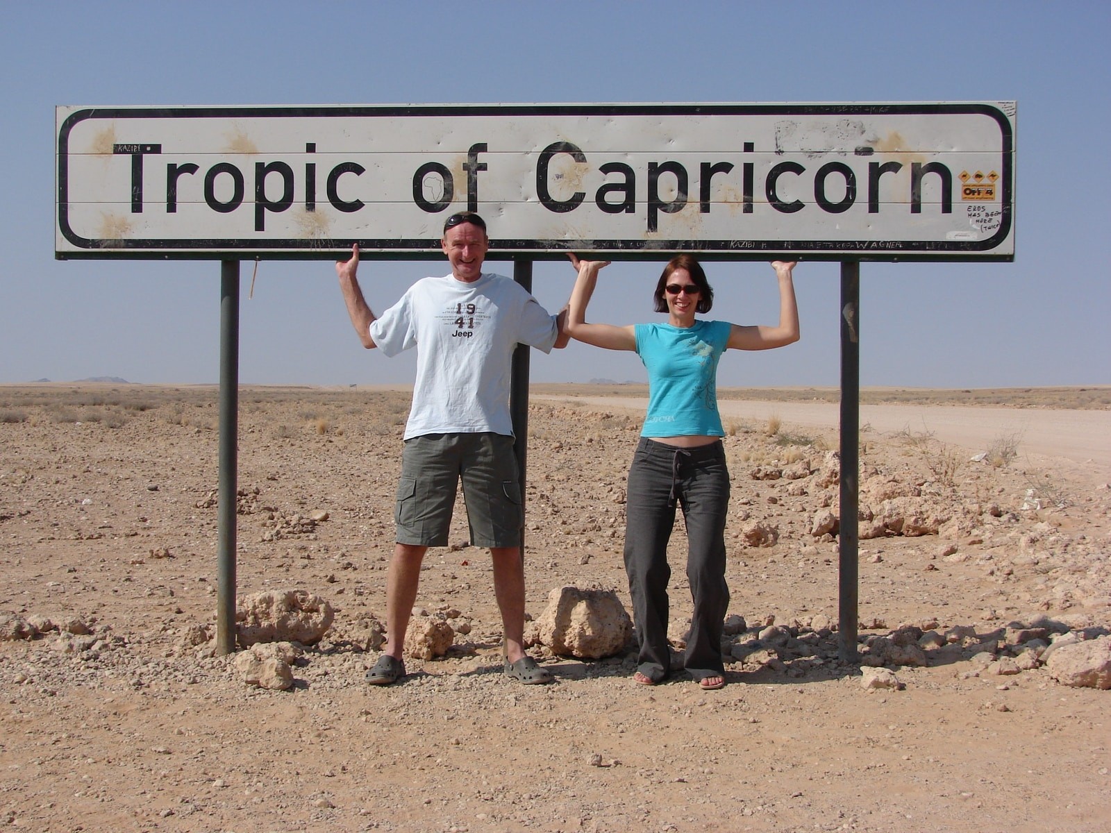 man and woman standing tropic of capricorn signage