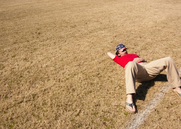 man in red top lying on lawn field during daytime