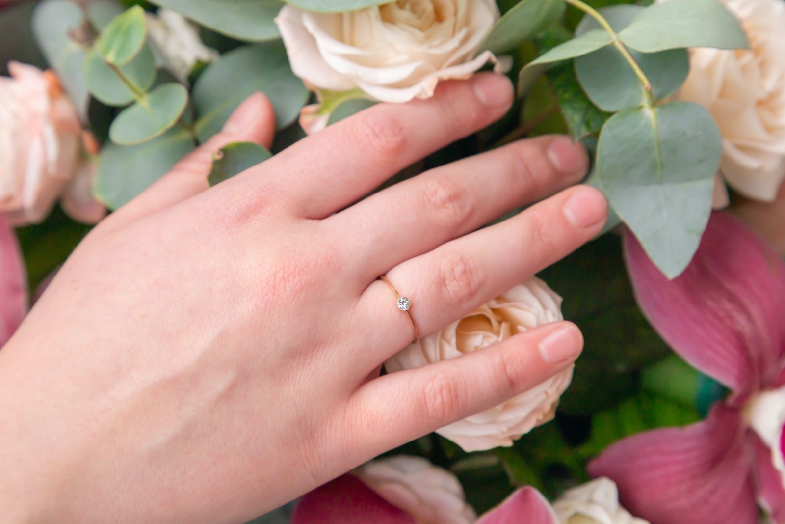person wearing gold wedding band holding white rose