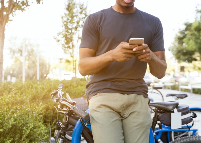 man holding smartphone leaning on bicycle during daytime
